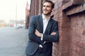 Smiling young male manager formal dressed leaning on a wall outdoors. Royalty Free Stock Photo