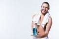 Smiling young man with bath towel around his neck holding bottle with tooth rinse in hands, Royalty Free Stock Photo