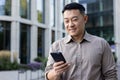 A smiling young man businessman Asian stands on the street of the city, holds a phone in his hand, writes a message Royalty Free Stock Photo