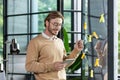 Smiling young man businessman, programmer, freelancer standing in the office, looking at a tablet, drawing a progress Royalty Free Stock Photo