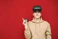 Smiling young man in casual clothes wears VR glasses, stands on a red background and points his finger at Copy space. Happy guy in Royalty Free Stock Photo