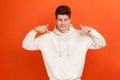 Smiling young man in casual style white hoodie pointing fingers down, showing on advertising area, free space for commercial Royalty Free Stock Photo