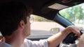 Smiling young man driving his car, turning the steering wheel and carefully looking at the road. Side view. Transport