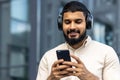 Smiling young man enjoying music on headphones while using smartphone outdoors Royalty Free Stock Photo