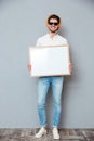 Smiling young man in hat and sunglasses holding white board Royalty Free Stock Photo