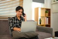 Smiling young man having phone conversation and working with laptop at home Royalty Free Stock Photo