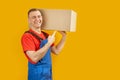 Smiling young man holding paper box. Young delivery man. Isolated on yellow background. Copy space, mock up Royalty Free Stock Photo