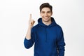 Smiling young man in hoodie, pointing finger up, showing advertisement, sale on top, standing over white background