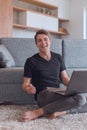 Smiling young man with laptop sitting on living room floor Royalty Free Stock Photo