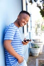 Smiling young man leaning against wall and holding cellphone Royalty Free Stock Photo