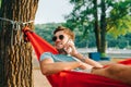 Smiling young man lies in a hammock at sunset in the park and calls on the phone with a smile on his face, looks away and laughs. Royalty Free Stock Photo