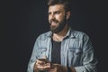 Smiling young man listening to favourite music on smartphone. Bearded hipster using wireless earphones. Portrait of male person Royalty Free Stock Photo