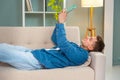 Smiling young man lying on sofa looking at social media with digital tablet. Indoors Royalty Free Stock Photo