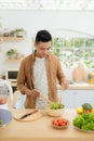 Smiling young man making vegetables salad in the kitchen at home