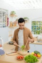 Smiling young man making vegetables salad in the kitchen at home