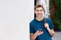 Smiling young man with mobile phone and backpack leaning against wall Royalty Free Stock Photo