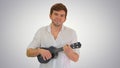 Smiling young man playing ukulele looking into the camera on gra Royalty Free Stock Photo