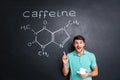 Smiling young man pointing on drawn caffeine molecule chemical structure