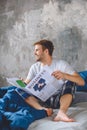 smiling young man reading business newspaper in bed during morning time