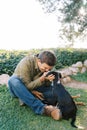 Smiling young man sits on the lawn and touches with his nose the nose of a big puppy Royalty Free Stock Photo