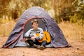 Smiling young man sitting near touristic tent and playing guitar in forest Royalty Free Stock Photo