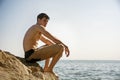 Smiling young man sitting on rock by sea or ocean Royalty Free Stock Photo
