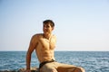 Smiling young man sitting on rock by sea or ocean Royalty Free Stock Photo