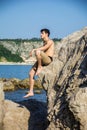 Smiling young man sitting on rock by sea or ocean Royalty Free Stock Photo