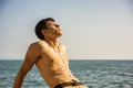 Smiling young man sitting by sea or ocean shore Royalty Free Stock Photo