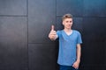 A smiling young man in a T-shirt shows a thumbs up against a gray wall background. Teen like it. Royalty Free Stock Photo