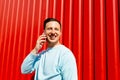 smiling young man talking on the mobile phone on the background of red wall Royalty Free Stock Photo