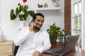 Smiling young man talking in phone and looking at his laptop Royalty Free Stock Photo