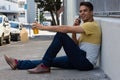 Smiling young man talking on smart phone while sitting on sidewalk