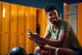 Smiling young man using smatphone in gym dressing room before workout Royalty Free Stock Photo