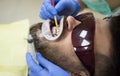 Smiling young man after visit dentist on bright blurred background. Dentist examining patient`s teeth in clinic