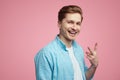 Smiling young man wearing blue shirt and is gesturing vsign over pink wall Royalty Free Stock Photo