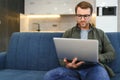 Smiling young man wearing glasses using laptop, sitting in cozy armchair, happy male looking at computer screen Royalty Free Stock Photo