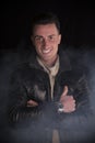 Smiling young man with white sweater and black leather jacket. Smoke and dark background Royalty Free Stock Photo