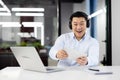 Smiling young man working in the office, sitting at a desk with a laptop, wearing headphones and playing online games on Royalty Free Stock Photo