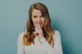 Smiling young millennial woman holding index finger on her lips over blue studio wall background Royalty Free Stock Photo