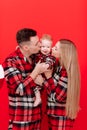 smiling young mother and father are kissing and hugging their baby boy on red background. concept of love and Royalty Free Stock Photo