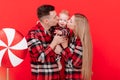 smiling young mother and father are kissing and hugging their baby boy on red background. concept of love and Royalty Free Stock Photo