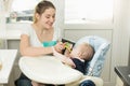 Smiling young mother feeding her baby in highchair Royalty Free Stock Photo