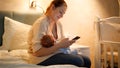 Smiling young mother feeding her newborn baby with breast milk working and browsing internet on smartphone at night in Royalty Free Stock Photo