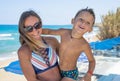 Smiling young mother kisses baby near the sea. Happy summer days.