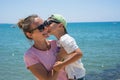 Smiling young mother kisses baby near the sea. Happy summer days. Royalty Free Stock Photo