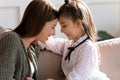 Smiling young mother touching foreheads with happy child daughter.