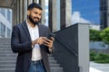 Smiling young Muslim male businessman using the phone while standing outside an office center Royalty Free Stock Photo
