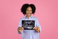 Smiling young pregnant african american curly lady in casual with big belly show ultrasound shot