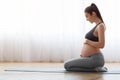 Pregnant woman training yoga at home, sitting on mat and touching belly Royalty Free Stock Photo